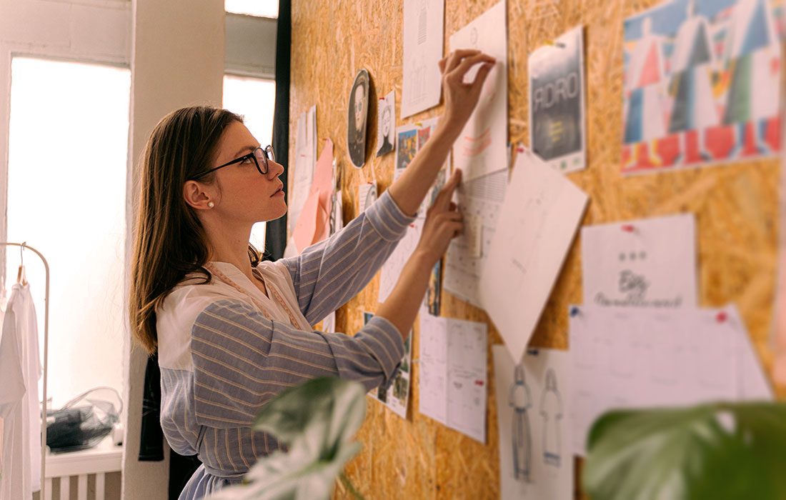 A designer standing at a wall of pinned concept sketches, pulling down the ideas that didn't make the cut.