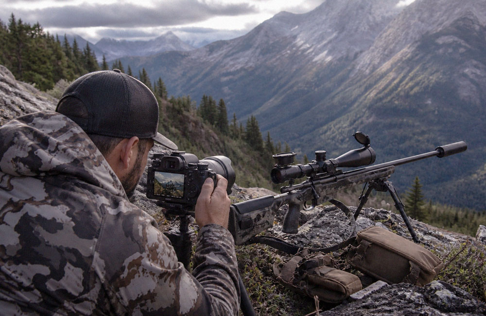 A content creator setting up a tripod and camera in a rugged mountain setting to film a product review under embargo.