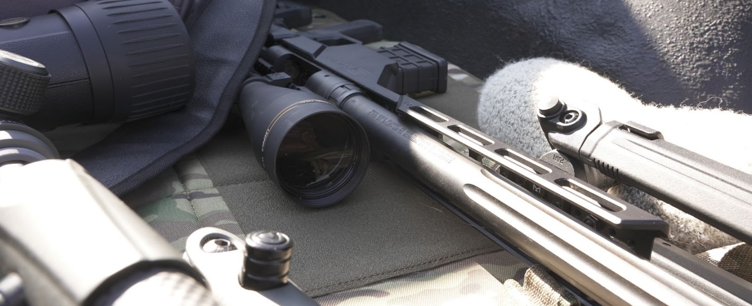 Photo of a leupold scope on a precision rifle laying down in the back of a truck with other gear.