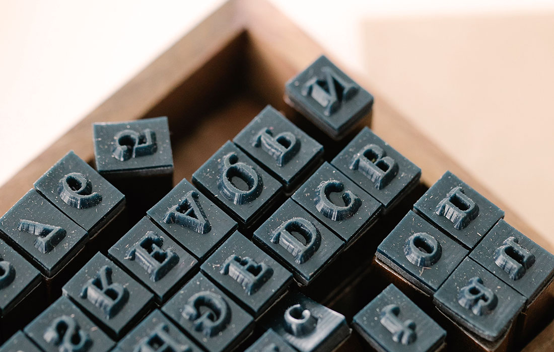 Rows of metal letterpress type next to a handwritten manuscript page, showing how written ideas were once reproduced by hand.
